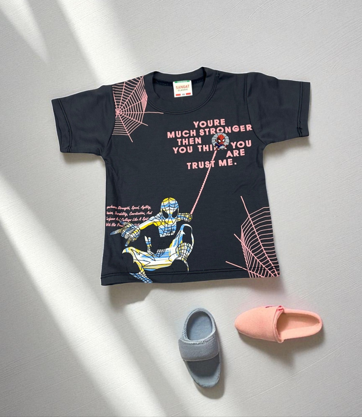 Black t-shirt with graphic designs and text on a light gray surface with two slippers.